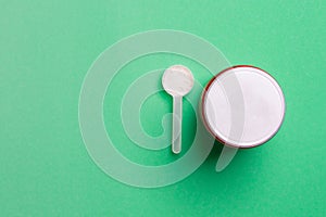 Red bank with powder and spoon on green colored paper background with copy space , top view