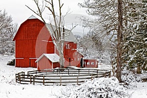 Red barn and circle fence enclosure covered in Winter white snow