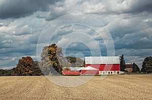 a red barn in a large field under cloudy skies with trees in the background