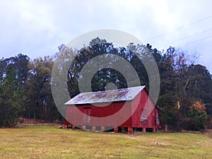 A red barn style building boarded up and abandoned distant view
