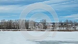 Red barn between trees on a cloudy winter day in Colorado with frozen lake in foreground
