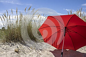 Red beach umbrella in the sand between dunes with blue summer sky