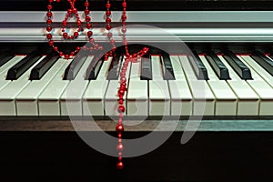 Red beads Christmas decoration lie casually on the piano keyboard