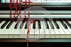 Red beads Christmas decoration lie casually on the piano keyboard