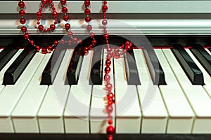 Red beads Christmas decoration lie casually on the piano keyboard