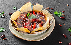 Red bean with nachos or pita chips, pepper and greens on plate over dark background. Mexican snack, Vegetarian food