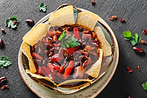 Red bean with nachos or pita chips, pepper and greens on plate over dark background. Mexican snack, Vegetarian food