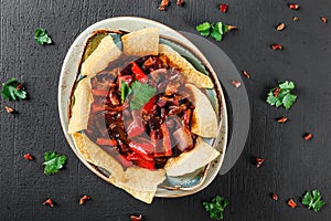 Red bean with nachos or pita chips, pepper and greens on plate over dark background. Mexican snack, Vegetarian food, top view