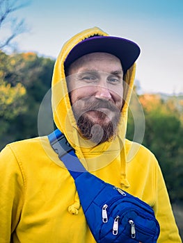 Red bearded millennial man with mustache in yellow hoody smiling portrait closeup Backpacker hiking climbing mountains