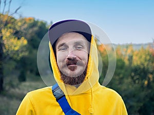 Red bearded millennial man with mustache in yellow hoody smiling portrait closeup Backpacker hiking climbing mountains