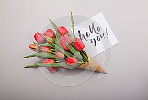 Red  beautiful tulips in an ice cream waffle cone with card Hello you on a concrete background. Conceptual idea of a flower gift.