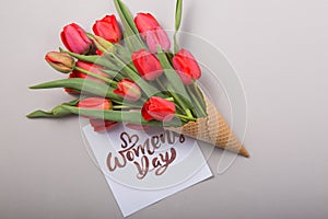 Red  beautiful tulips in an ice cream waffle cone with card Womans Day on a concrete background. Conceptual idea of a flower gift