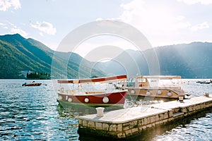 Red and beige pleasure boats on the water at the pier in the town of Perast.