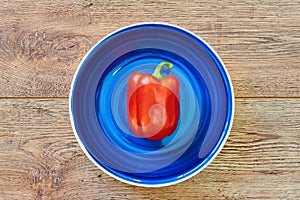 Red bell pepper on a blue plate on a wooden tabletop