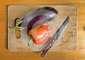 Red bell pepper, eggplant and knife on wooden cutting board