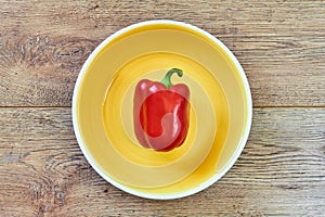 Red bell pepper on a yellow plate on a wooden tabletop