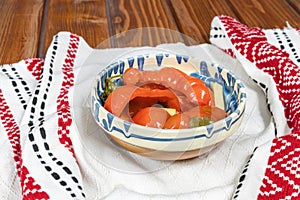 Red bell peppers pickled in Romanian traditional clay bowl and traditional towel on wooden table