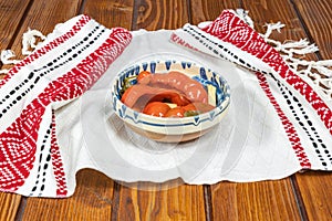 Red bell peppers pickled in Romanian traditional clay bowl and traditional towel on wooden table