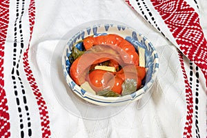 Red bell peppers pickled in Romanian traditional clay bowl and traditional towel on wooden table