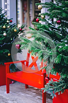 Red bench surrounded by decorated christmas trees, lights and snow