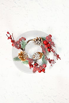 Red berries with fir branches and cones. Christmas wreath on white background with snow. New year card