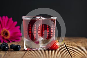 Red berries liqueur in shot glass isolated on black background and wooden table. Homemade alcohol drink concept.