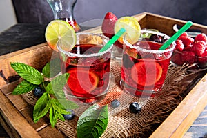 Red berry cocktail with ice. Raspberry, lime, strawberry, blueberry and mint leaves. Berry mojito in misted glasses