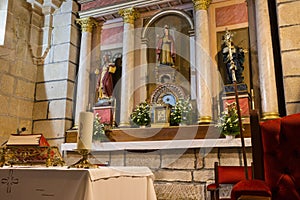 Red Bible and candle on altar table with saint sculptures and red chair. Faith and religion concept. Church interior with altar.