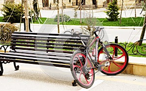 A red bicycle standing parked in a bike stand close to wooden bench. Street is made of blocks of granite