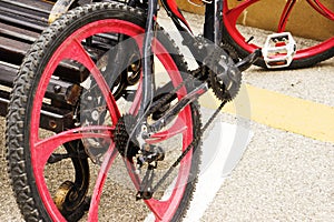 A red bicycle standing parked in a bike stand close to wooden bench. Street is made of blocks of granite