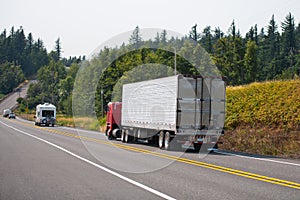 Red big rig cab-over semi truck transporting cargo in refrigerator semi trailer on the hills road