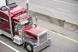 Red big rig classic semi truck tractor with chrome accessories and roof horns running with cargo in refrigerated semi trailer on