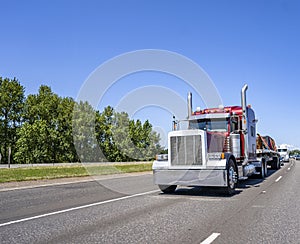 Red big rig classic semi truck tractor with chrome accessories and vertical pipes transporting tightened by slings load on flat