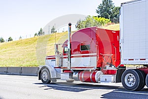 Red big rig long cab classic semi truck transporting frozen cargo in reefer semi trailer driving on the road in sunny day