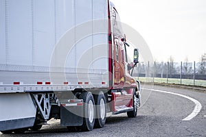 Red big rig long haul semi truck transporting dry van semi trailer turning on the local road