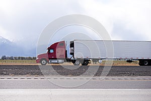 Red big rig semi truck carry refrigeration semi trailer and going by flat road in Utah