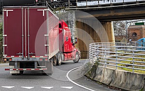 Red big rig semi truck with dry van semi trailer driving on the road and turning under the bridge