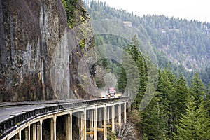 Red big rig semi truck with flat bed semi trailer running on the wet road with rain dust driving on the overpass bridge on the