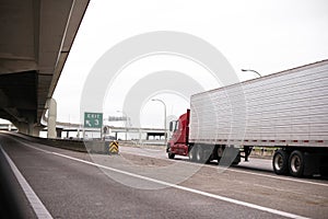 Red big rig semi truck with long reefer trailer transporting fro