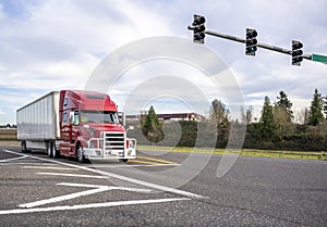Red big rig semi truck with powerful aluminum grille guard transporting cargo in dry van semi trailer standing on the crossroad