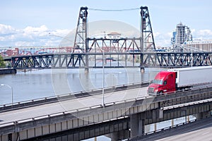 Red big rig semi truck with refrigerator semi trailer transporting cargo on highway overpass intersection along the Willamette Ri