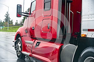 Red big rig semi truck with semi trailer running on the wet road in rain weather