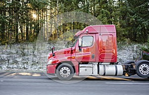 Red big rig semi truck tractor going on the road with green forest on background