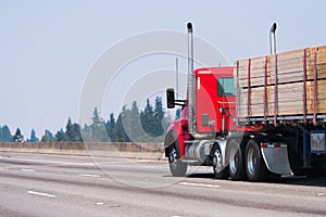 Red big rig semi truck transport timber on flat bed semi trailer