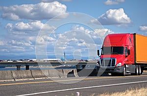 Red big rig semi truck transporting container on the road with r