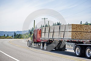 Red big rig semi truck transporting wood lumber on the flat bed semi trailer running on the turning road