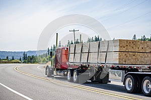 Red big rig semi truck transporting wood lumber on the flat bed semi trailer running on the turning road photo