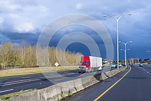 Red big rig semi truck with two semitrailers driving on divided multiline highway