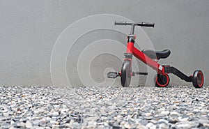A red bike for children with cement wall behide at home. Mother teaching his son to ride a bike