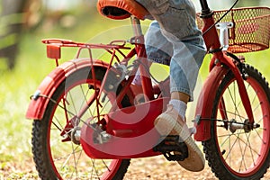 red bike close-up children's legs wearing jeans and wear pink sneakers Riding in the outdoor